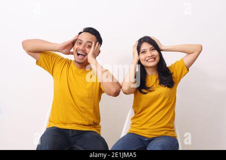 Cheerful asian couple sat with hands holding their heads with a happy expression. Isolated on white background with copyspace