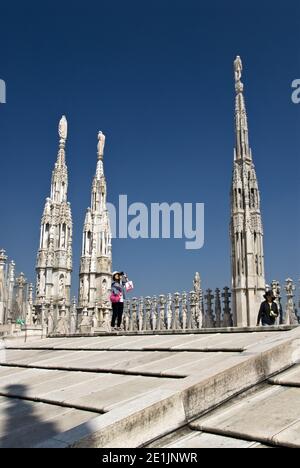 Tourists photograph the cathedral architecture and city skyline from the roof of Milan Cathedral (Duomo di Milano), Milan, Italy.