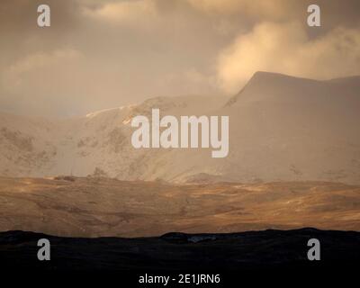 dramatic evening light through stormy clouds illuminates snow on Kidsty Pike & High Street in golden hour Cumbrian landscape in England, UK Stock Photo