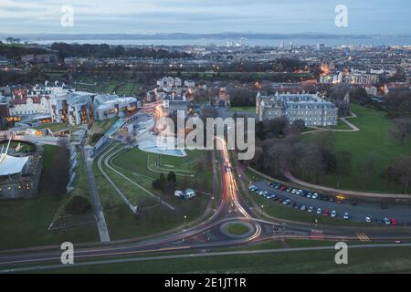 A sweeping evening view from Salisbury Crags over the modern architecture of the Scottish Parliament Building across from Holyrood Palace at the base Stock Photo