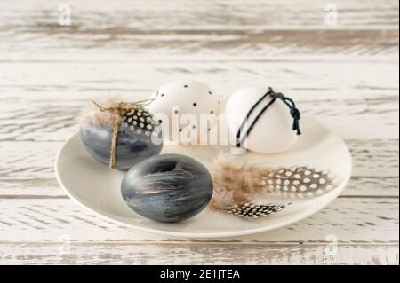 Trendy colored easter eggs in dark colors and feathers on a plate on wooden table. Preparation for easter holidays. Fesstive composition Stock Photo