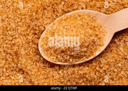 Wooden spoon full of light brown granulated sugar on top of brown granulated sugar. Stock Photo