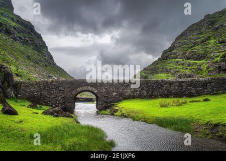 Small stone Wishing Bridge over winding stream in green valley, Gap of Dunloe in Black Valley, Ring of Kerry, County Kerry, Ireland Stock Photo
