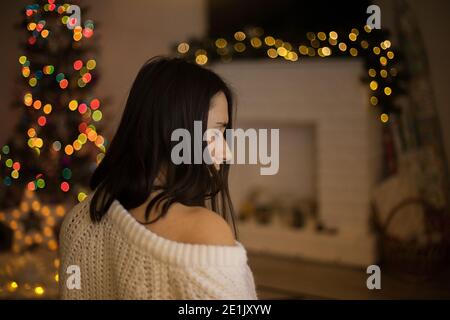 woman back in white sweater smiling and in front of christmas tree and fireplace Stock Photo
