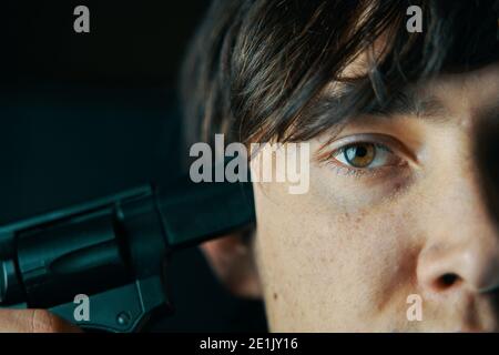 Young man put the muzzle of gun to his temple. Guy is going to commit suicide. Male wants to shoot himself with a pistol. Stock Photo