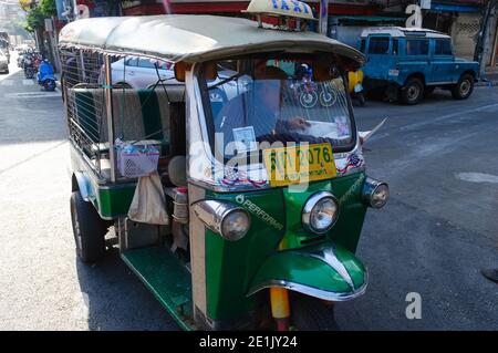 Bangkok, Thailand - December, 2015: Green tuk tuk taxi parked on the street and waiting for tourists. Tuk-tuk driver sitting inside and reading newspa Stock Photo