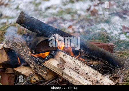 An outdoor fire burns in a small pile of logs in the winter, with snow visible on the ground behind it. Stock Photo