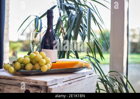 cheese platter with grapes and wine on a table near a window with a cozy chair. Modern interior design Stock Photo