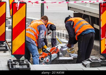 Back view of workers wearing reflective vest cutting and repairing street curbs in Bucharest, Romania, 2020 Stock Photo