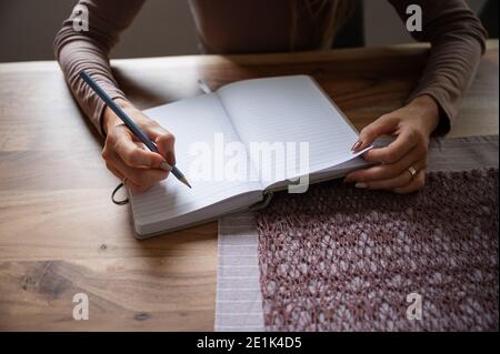 Woman writing in blank notepad with a pencil on wooden dinning table. Conceptual of working or studying from home. Stock Photo