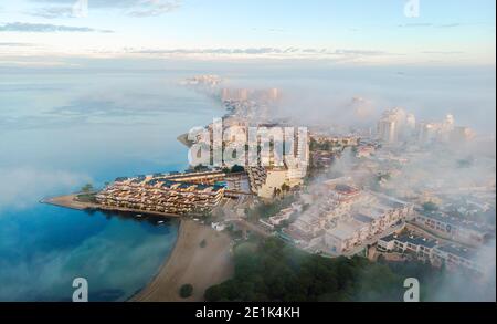 Aerial drone point of view La Manga del Mar Menor cityscape and Mediterranean sea during sunrise, cloudy misty sky, picturesque scenery. Travel, beaut Stock Photo