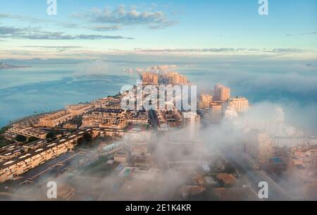 Aerial drone point of view La Manga del Mar Menor cityscape and Mediterranean sea during sunrise, cloudy misty sky, picturesque scenery. Travel, beaut Stock Photo