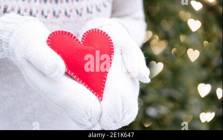 Red heart in hands. Love declaration concept. A girl in mittens stretches out her hands in which a cute hand-sewn heart lies on a background with boke Stock Photo