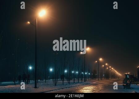 Urban alley in foggy winter night illuminated by street lamps. Stock Photo