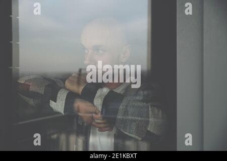 Sad young man looking through the window. Stock Photo