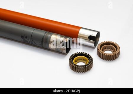 the old worn out heating shaft from the laser printer lies next to the new one and with gears on a clean white background Stock Photo
