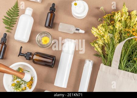 Various bottles, tubes, jar with cosmetic, wildflowers in eco textile bag, mortar bowl with pestle on beige background. Concept natural herbal organic Stock Photo