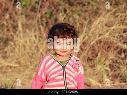 Indian beautiful little male child photo in which child stands outside in nature and out of focus background with portrait photo of indian child , Stock Photo