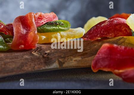 Dried fruits: Yellow candied pineapple rings, red papaya and green on a wooden cutting board on gray concrete Stock Photo