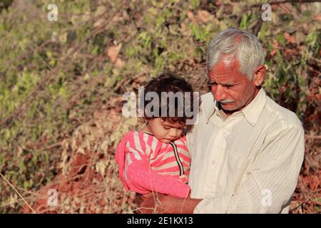 An Indian small child with an Indian grandfather sitting in the grandfather's lap enjoying nature, india Stock Photo