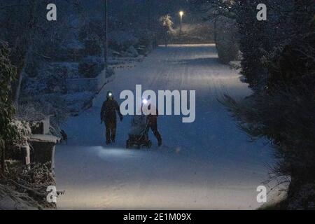 Flintshire, North Wales, UK 8th January 2021, UK Weather:  Freezing overnight temperatures have left many waking to well below zero temperatures this morning with heavy snowfall in the area too causing treacherous driving conditions. A couple pushing a pram in the heavy snowfall this morning in the village of Lixwm at dawn© DGDImages/Alamy Live News Stock Photo