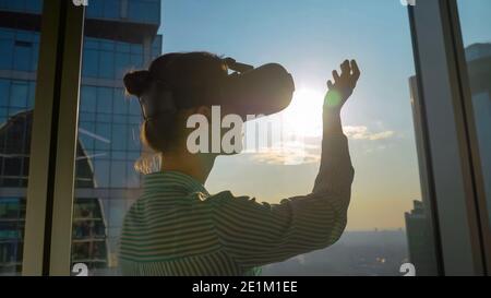 Woman using VR headset against skyscraper window in office Stock Photo