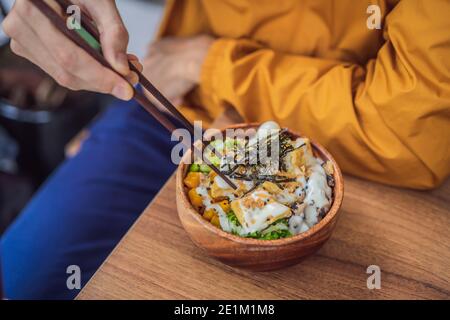 Man eating Raw Organic Poke Bowl with Rice and Veggies close-up on the table. Top view from above horizontal Stock Photo