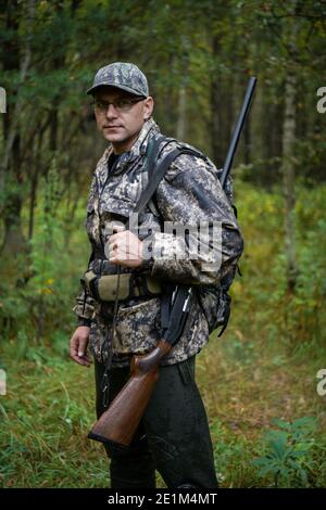 Man hunter standing with shotgun rifle outdoors preparing for bird hunt in autumn forest. Stock Photo