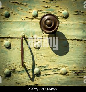 Rusty door handle on an aged wooden wall with a vintage green paint finish and rivets. France Stock Photo