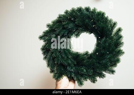 Male hand holding green christmas wreath from fir tree against white background - decorations includes small light bulbs Stock Photo