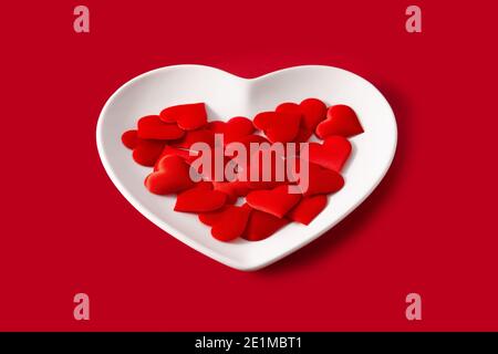 Heart shaped plate with red hearts inside on red background Stock Photo
