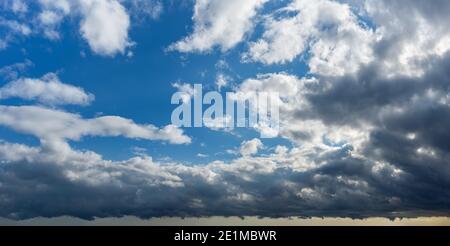 Storm is coming. Dark gray stormy clouds covering bright blue sky with fluffy white clouds. Changing weather from clear sunny to rainy overcast. Stock Photo