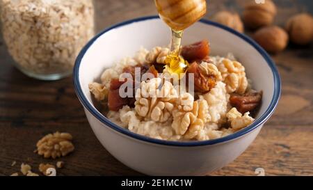 Oatmeal porridge with dried fruits and walnuts and honey. Adding honey to healthy breakfast porridge oats Stock Photo