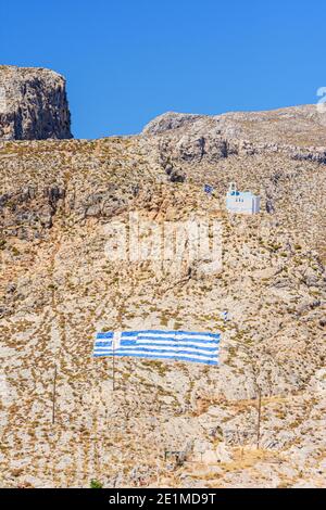 Greek flag and white church on the dry barren hills that overlook Kalymnos Island, Dodecanese, Greece Stock Photo