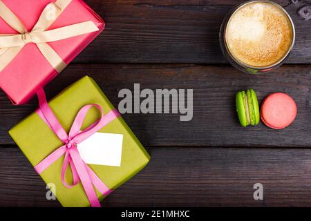 Two boxes wrapped in gift paper, a glass of latte and a few French macarons on a dark table. View from above. Stock Photo