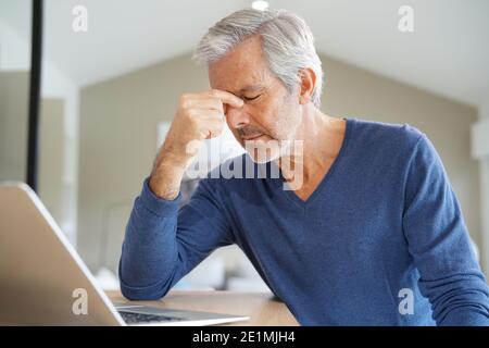 Senior man having a headache while working on laptop computer Stock Photo