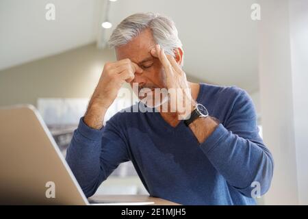 Senior man having a headache while working on laptop computer Stock Photo