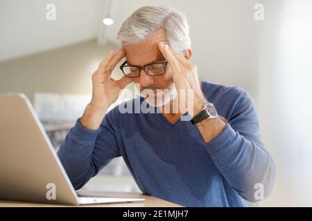 Senior man having migraine while working on laptop computer Stock Photo