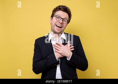 Happy caucasian man in suit being content to hear compliment, expresses his gratitude and thanks, keeps hands on heart. Positive cheerful male Stock Photo