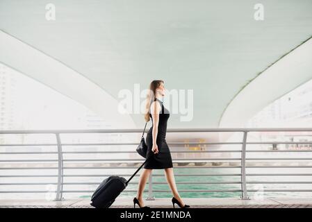 Young modern confident business woman pulling a suitcase in a Dubai Marine. Starting a new job in a big city. Stock Photo