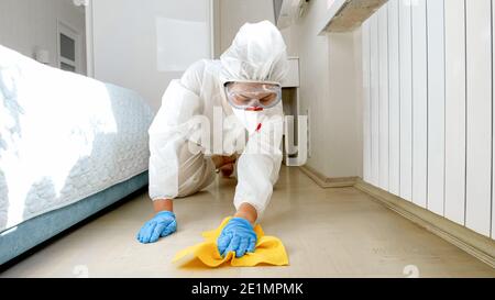 Housewife wearing protective medical suit wasing and cleaning floor at home. Desinfection and hygiene during lockdown and staying at home at pandemic Stock Photo