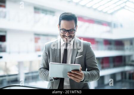 Happy successful businessman using smart phone while leaning on the glass fence. In background business center. Stock Photo