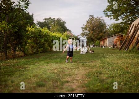 Happy playful little boy running thru the backyard on his grandparents animal farm. Happy childhood. Stock Photo