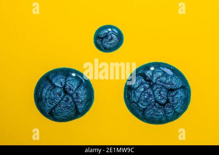 Blue sparkly paint drops on yellow background Stock Photo