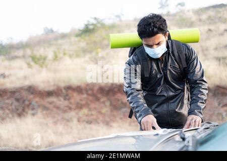 Young man in face mask busy searching or checking map on car before starting the hiking - concept of solo travel with safety measures due to coronavir Stock Photo