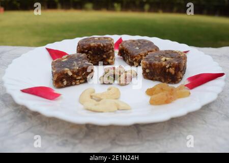 Khajur ka halwa or khajoor paak is a traditional Indian and Pakistani dish. dry fruit halwa barfi dates decorated with red pink rose petals and served Stock Photo