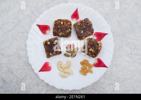 Khajur ka halwa or khajoor paak is a traditional Indian and Pakistani dish. dry fruit halwa barfi dates decorated with red pink rose petals and served Stock Photo