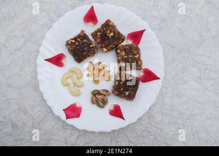 Khajur ka halwa or khajoor paak is a traditional Indian and Pakistani dish. dry fruit halwa barfi dates decorated with red pink rose petals and served Stock Photo