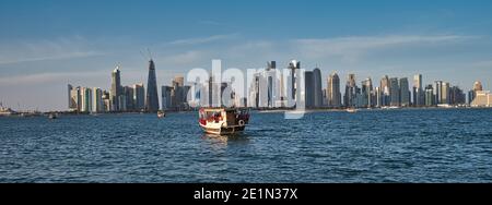 Doha skyline from the corniche promenade afternoon shot showing dhows with Qatar flag in Arabic gulf in foreground and clouds in the sky in background Stock Photo