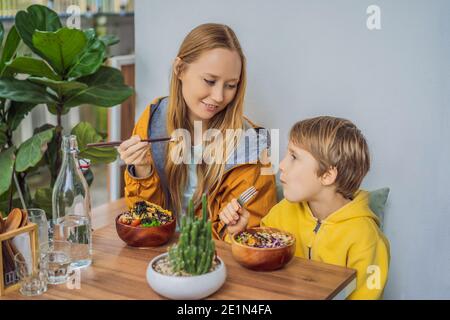 Mother and son eating Raw Organic Poke Bowl with Rice and Veggies close-up on the table. Top view from above horizontal Stock Photo